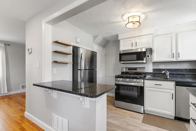 kitchen featuring visible vents, a peninsula, white cabinetry, a sink, and stainless steel appliances