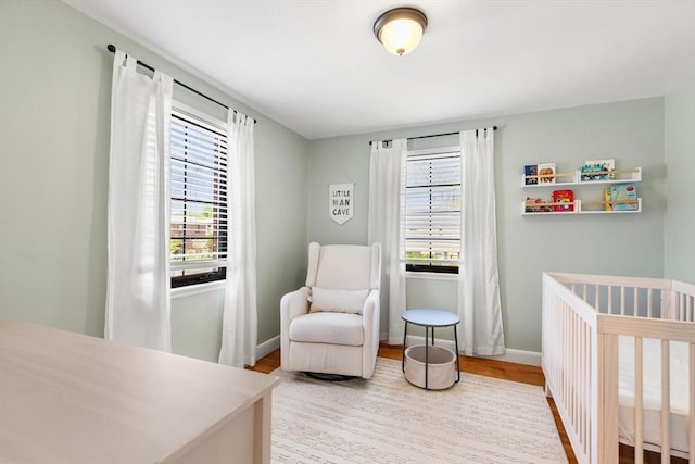 bedroom with a crib, multiple windows, baseboards, and wood finished floors