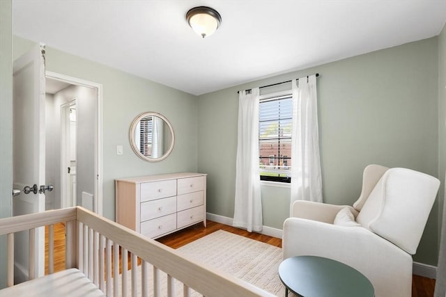 bedroom featuring a nursery area, baseboards, and dark wood-style floors