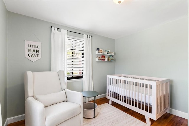 bedroom with baseboards, a crib, and wood finished floors