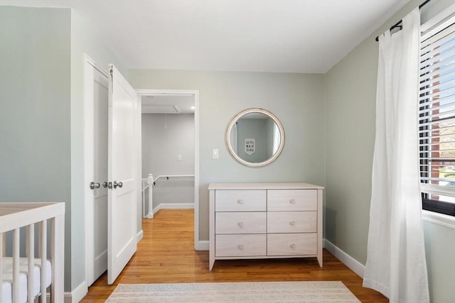 bedroom with baseboards, attic access, a crib, and wood finished floors
