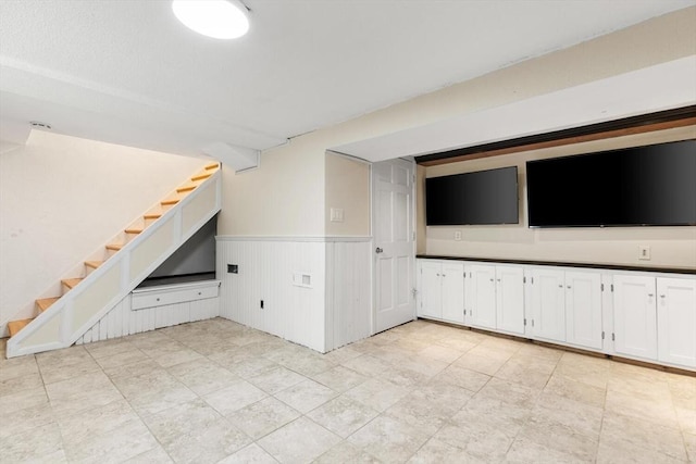 unfurnished living room featuring stairway and a wainscoted wall