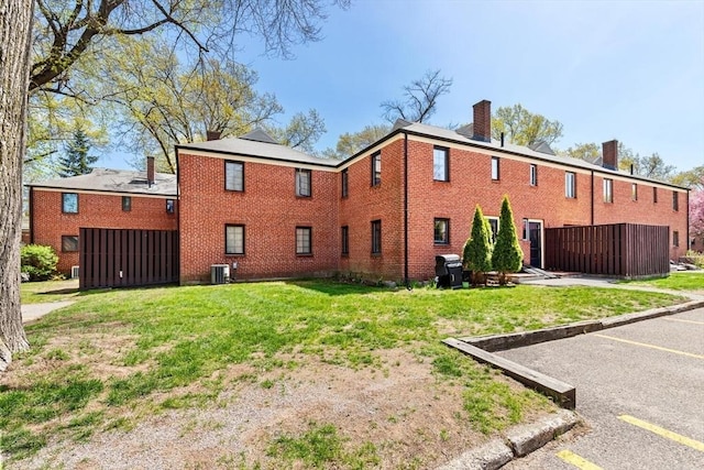 rear view of property featuring brick siding, uncovered parking, a lawn, and a chimney