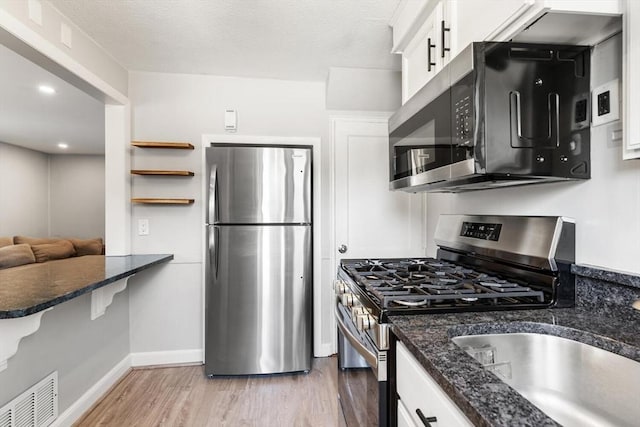 kitchen featuring visible vents, baseboards, white cabinets, light wood-style floors, and stainless steel appliances