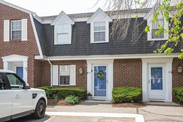 townhome / multi-family property with uncovered parking, brick siding, and a gambrel roof