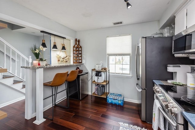 kitchen featuring appliances with stainless steel finishes, a breakfast bar, baseboards, and dark wood-style floors