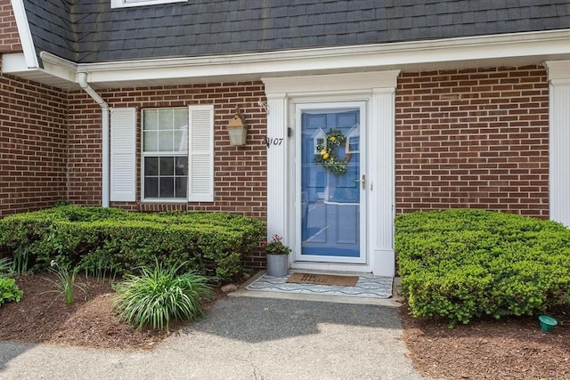 doorway to property with a shingled roof, mansard roof, and brick siding