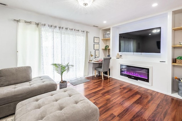 living room with visible vents, built in features, a glass covered fireplace, wood finished floors, and recessed lighting