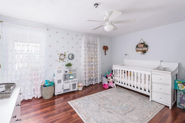 bedroom with a nursery area, ceiling fan, and wood finished floors