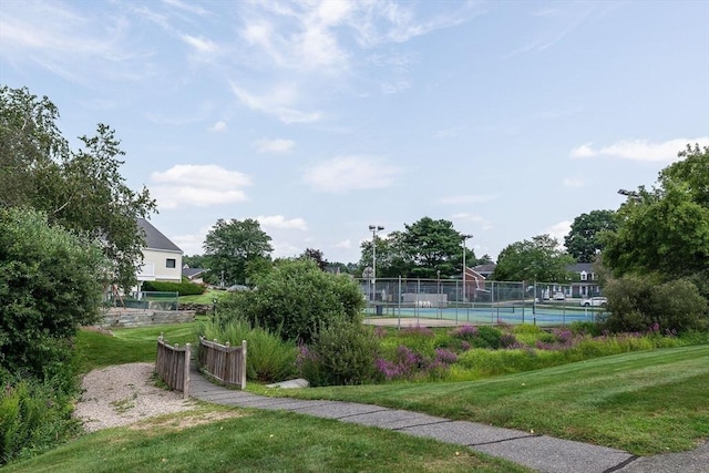 view of property's community with a tennis court, fence, and a yard