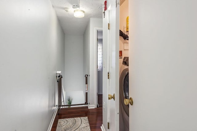 hallway featuring a textured ceiling, wood finished floors, washer / dryer, and baseboards