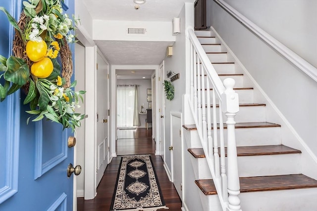 entrance foyer featuring stairway, visible vents, and dark wood-type flooring