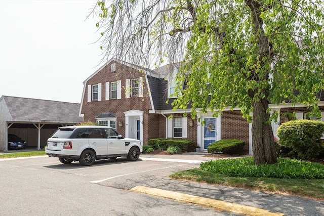 colonial inspired home featuring brick siding, a shingled roof, uncovered parking, and a gambrel roof