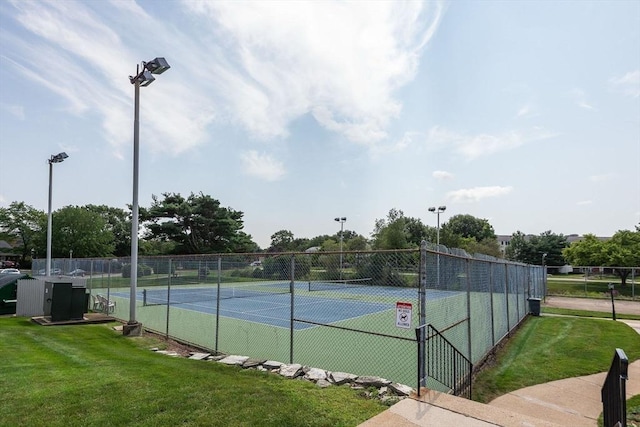 view of tennis court with a lawn and fence