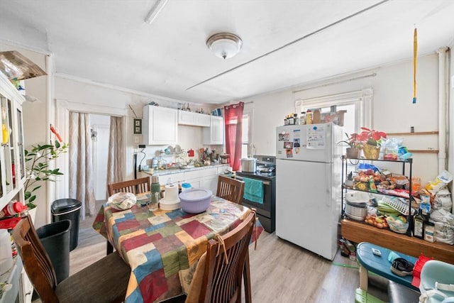 kitchen with stainless steel electric stove, white cabinets, light wood-type flooring, and white fridge