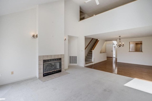 unfurnished living room featuring visible vents, high vaulted ceiling, a notable chandelier, carpet flooring, and stairs