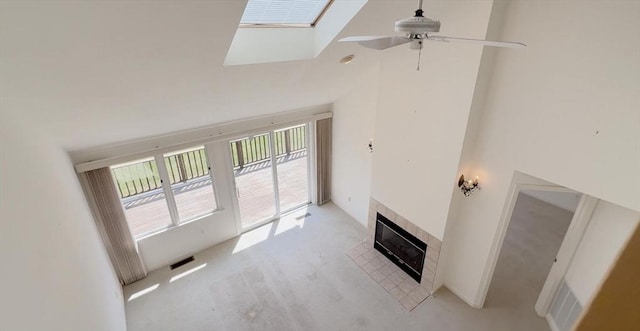 unfurnished living room with visible vents, ceiling fan, a high ceiling, a tiled fireplace, and a skylight