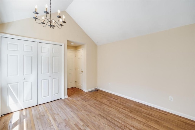 unfurnished bedroom with an inviting chandelier, light wood finished floors, high vaulted ceiling, baseboards, and a closet