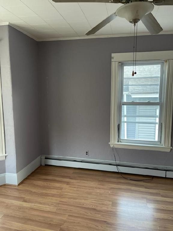 empty room featuring light wood-type flooring, a baseboard radiator, a wealth of natural light, and crown molding