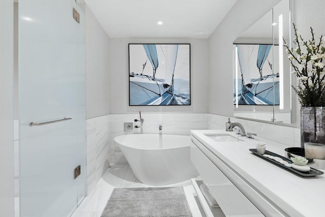 bathroom with vanity, a tub to relax in, and tile walls