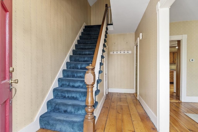 stairway featuring wood-type flooring and wallpapered walls