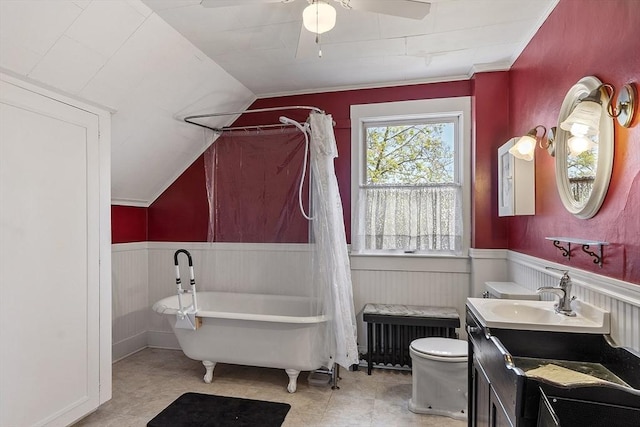 bathroom with a freestanding bath, radiator, a wainscoted wall, and lofted ceiling