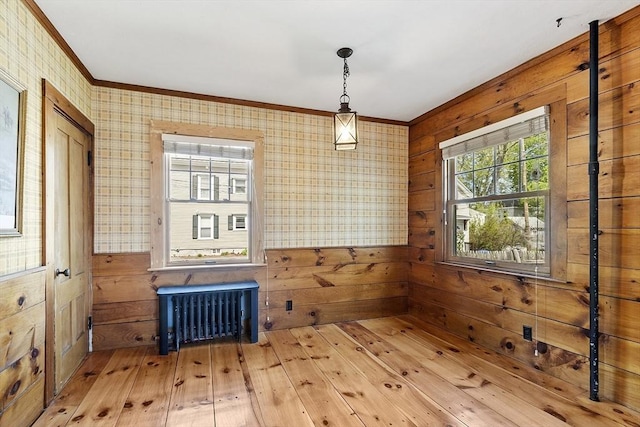 empty room with wood-type flooring, ornamental molding, radiator heating unit, wooden walls, and wallpapered walls