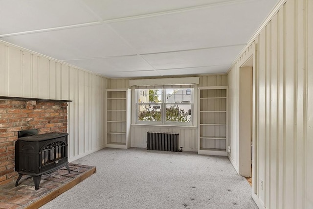 unfurnished living room featuring carpet flooring, radiator heating unit, and a wood stove