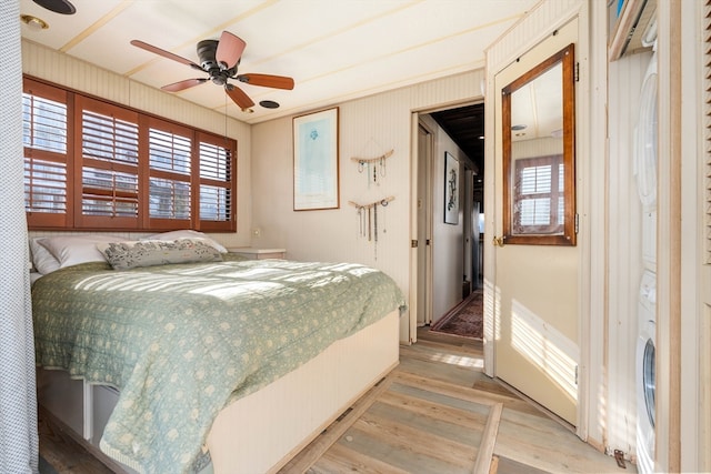 bedroom with ceiling fan, hardwood / wood-style flooring, and stacked washer and clothes dryer