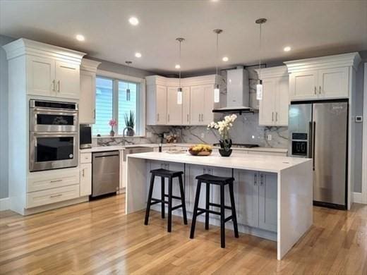 kitchen with wall chimney exhaust hood, decorative light fixtures, a center island, stainless steel appliances, and white cabinets