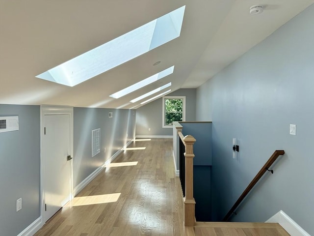 additional living space featuring vaulted ceiling with skylight and light wood-type flooring