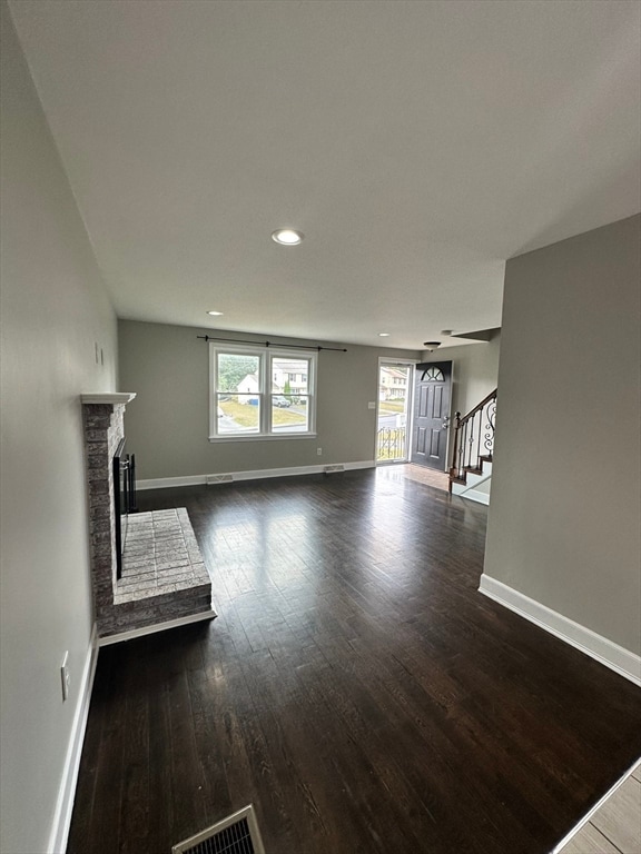 unfurnished living room with a stone fireplace and dark hardwood / wood-style flooring