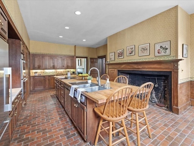 kitchen featuring a breakfast bar, sink, a center island with sink, stainless steel double oven, and backsplash