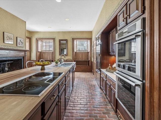 kitchen featuring butcher block counters, sink, a large fireplace, stainless steel double oven, and black electric cooktop