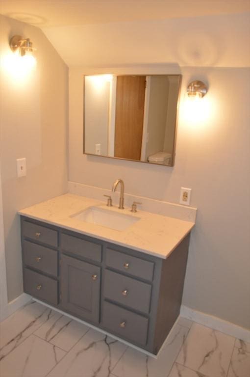 bathroom featuring marble finish floors, baseboards, vanity, and vaulted ceiling