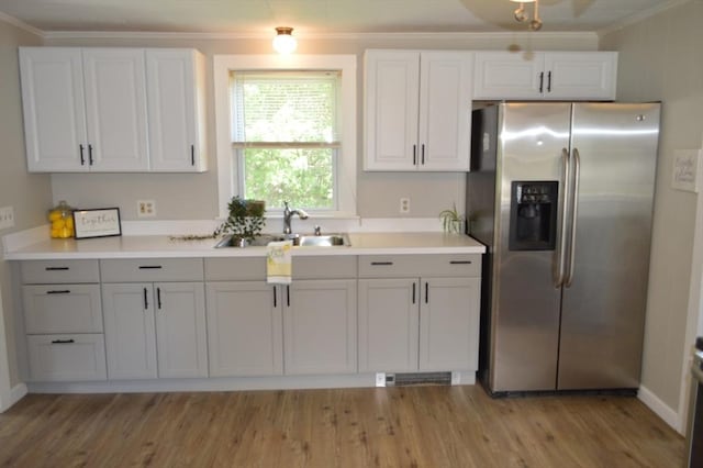 kitchen featuring stainless steel fridge with ice dispenser, a sink, ornamental molding, light wood-style floors, and light countertops