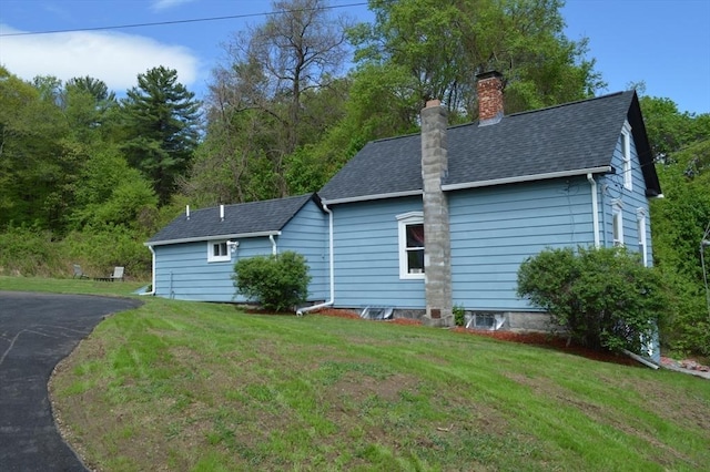 view of side of property featuring a chimney, a lawn, and a shingled roof