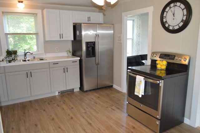 kitchen with stainless steel appliances, a sink, light wood finished floors, ornamental molding, and light countertops