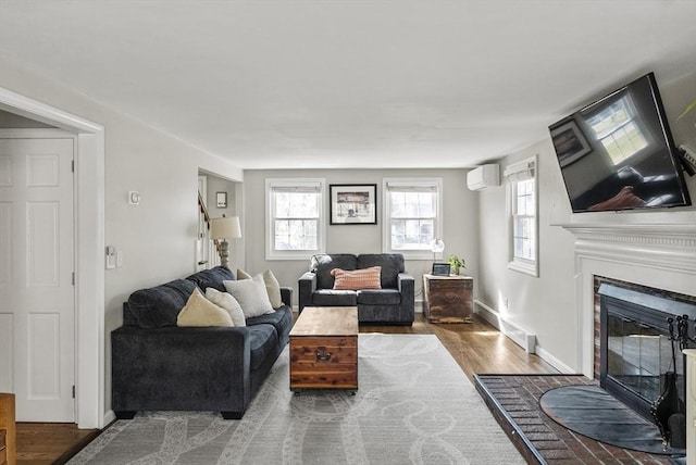 living area featuring an AC wall unit, a glass covered fireplace, a healthy amount of sunlight, and wood finished floors