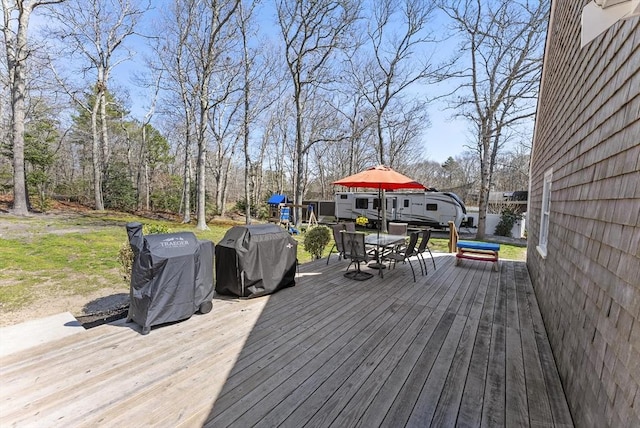 wooden deck featuring outdoor dining area, a playground, and a grill