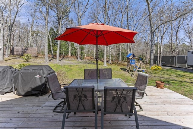 wooden deck featuring a playground, a yard, area for grilling, and outdoor dining space