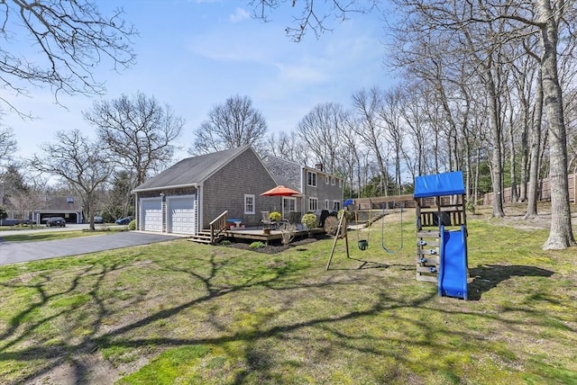 view of yard with a detached garage, a deck, a playground, and aphalt driveway