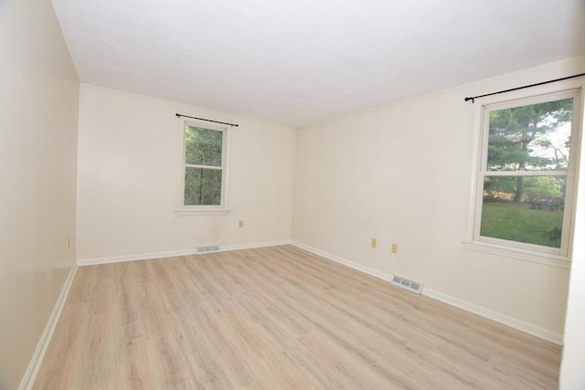 empty room featuring plenty of natural light, light wood-style floors, and baseboards