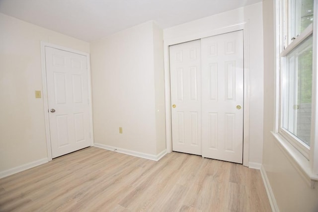 unfurnished bedroom featuring light wood-style floors, baseboards, and a closet