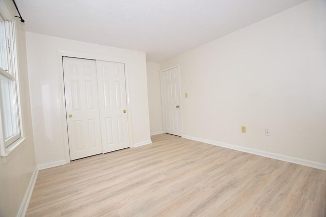 unfurnished bedroom with light wood-type flooring, a closet, and baseboards