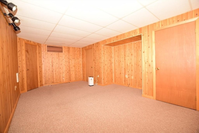 carpeted empty room with a drop ceiling and wooden walls