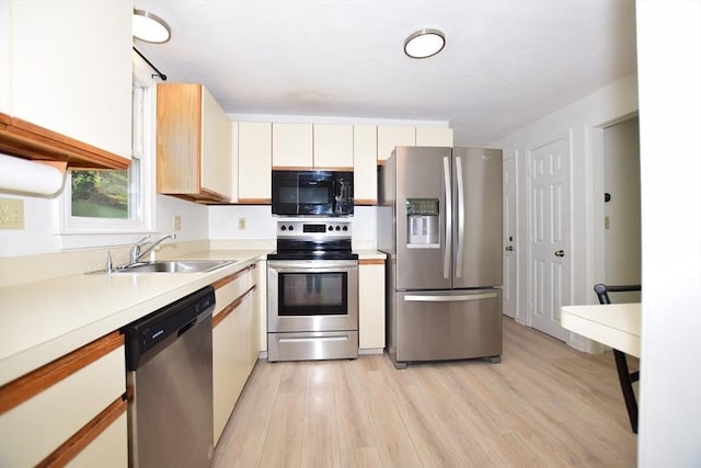 kitchen with appliances with stainless steel finishes, a sink, light wood-style flooring, light countertops, and white cabinetry