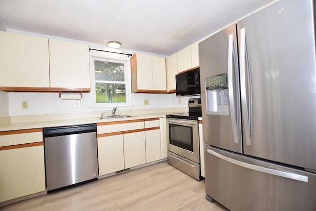 kitchen featuring stainless steel appliances, a sink, light wood-style floors, light countertops, and cream cabinetry