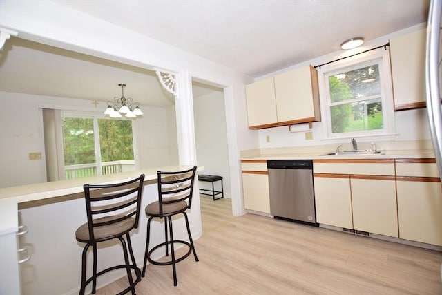 kitchen featuring stainless steel dishwasher, a sink, light countertops, light wood-type flooring, and a chandelier