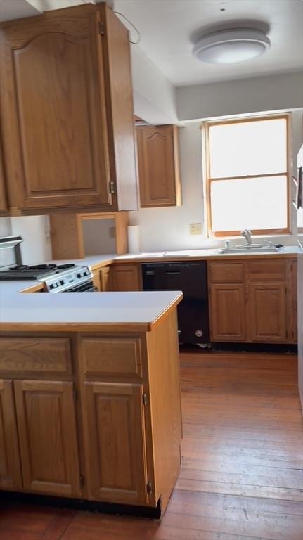 kitchen with dark wood-style floors, black dishwasher, light countertops, a sink, and a peninsula